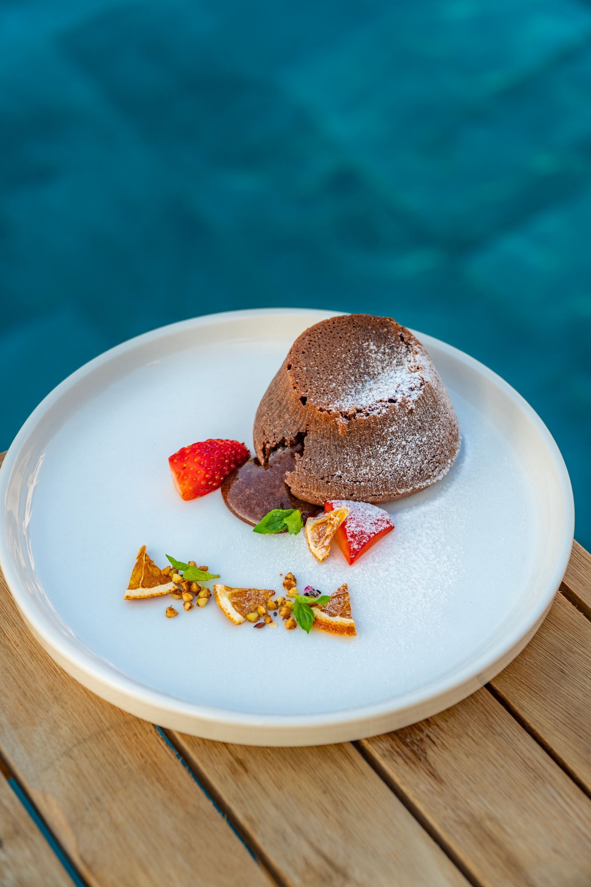 A white plate topped with a chocolate cake and strawberries on a wooden table.