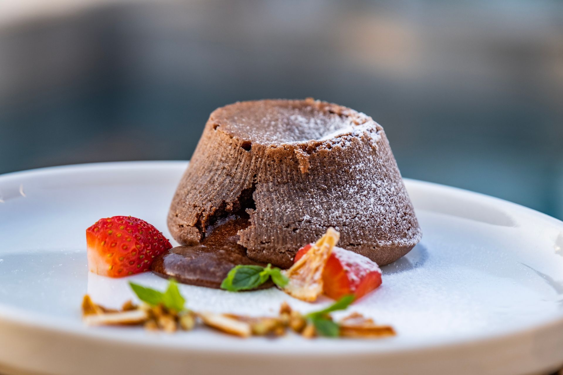 A chocolate lava cake with strawberries and almonds on a white plate.