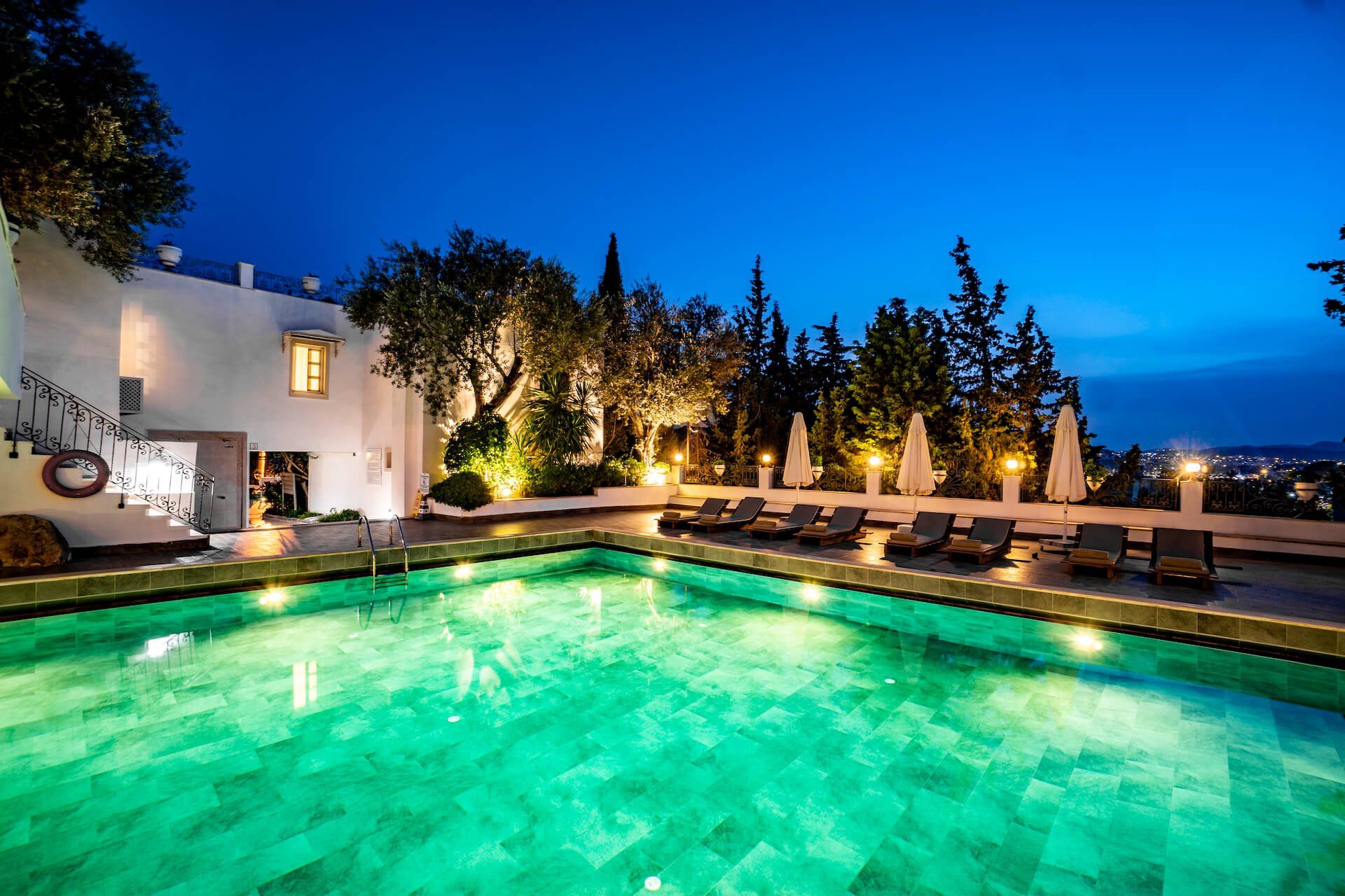 A large swimming pool is lit up at night in front of a white building.