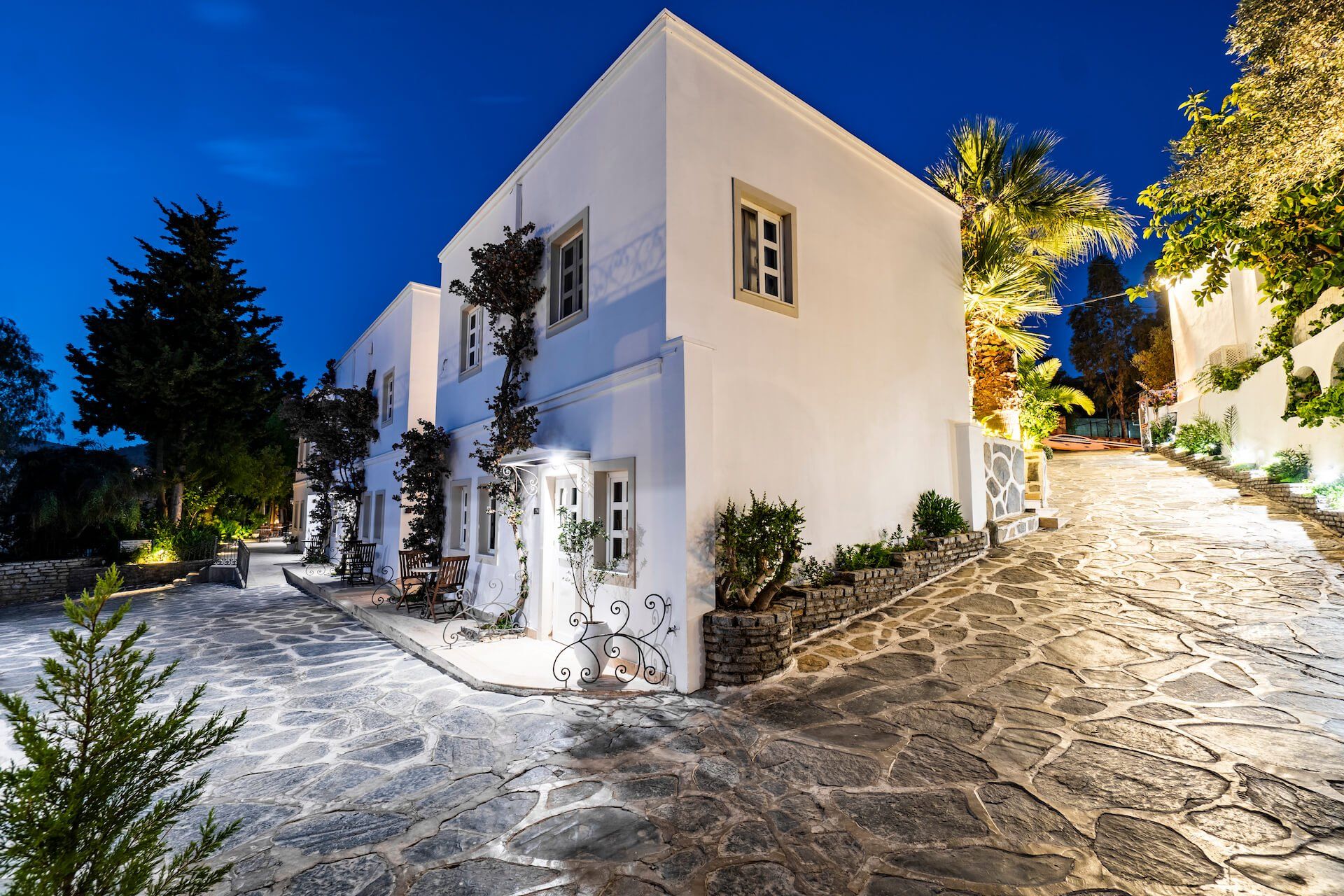 A white building with a stone driveway leading to it is lit up at night.