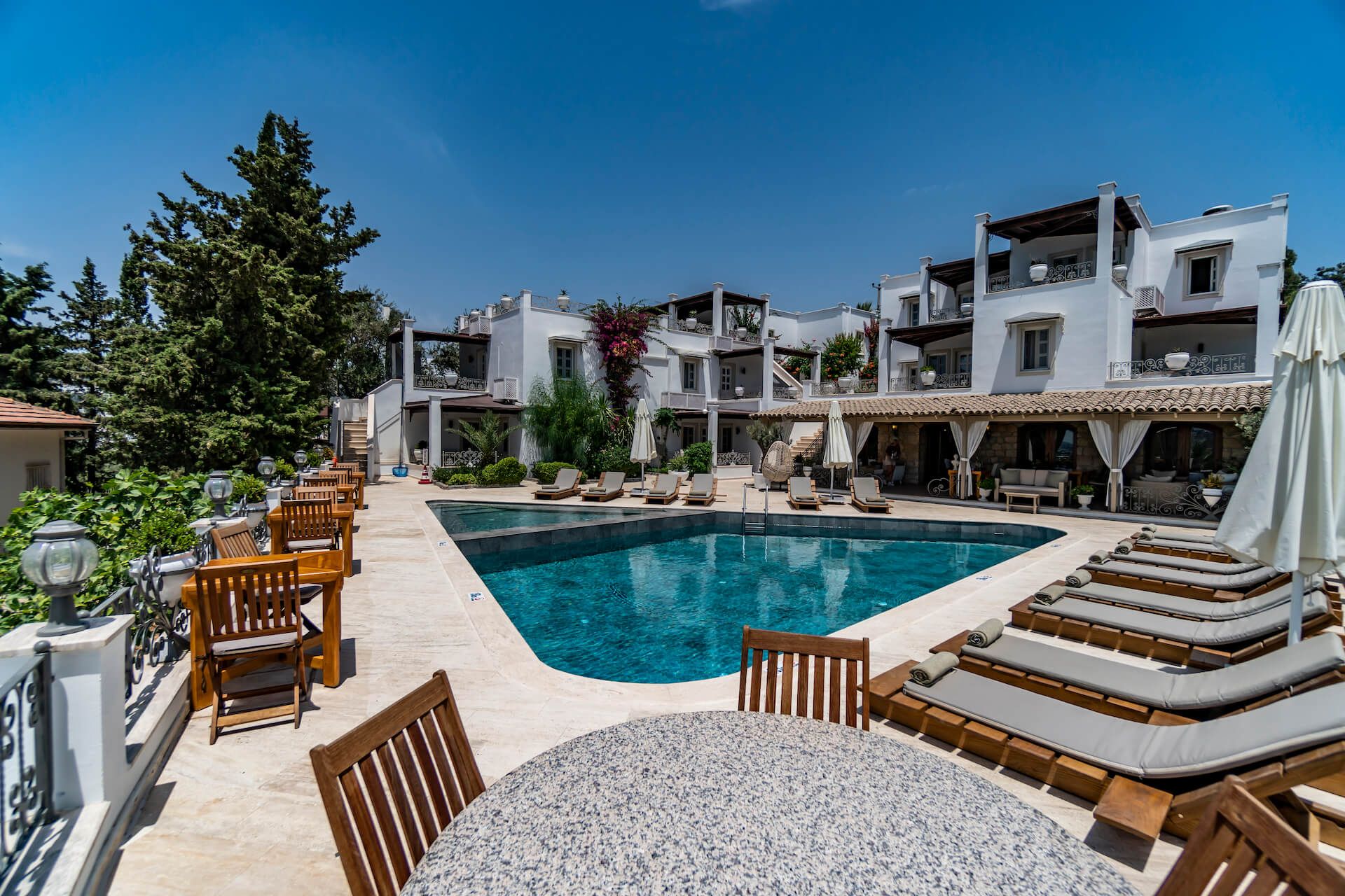 A large swimming pool surrounded by chairs and umbrellas in front of a building.