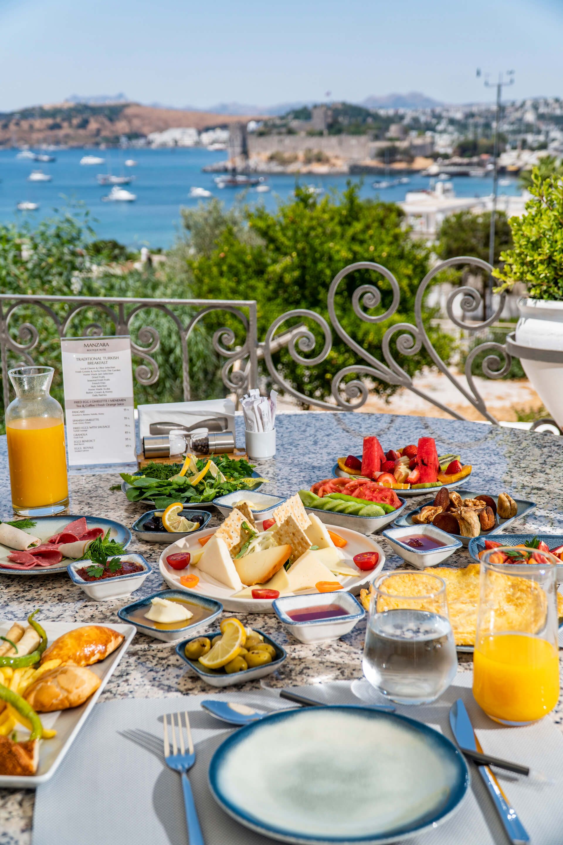 A table topped with plates of food and drinks with a view of the ocean.