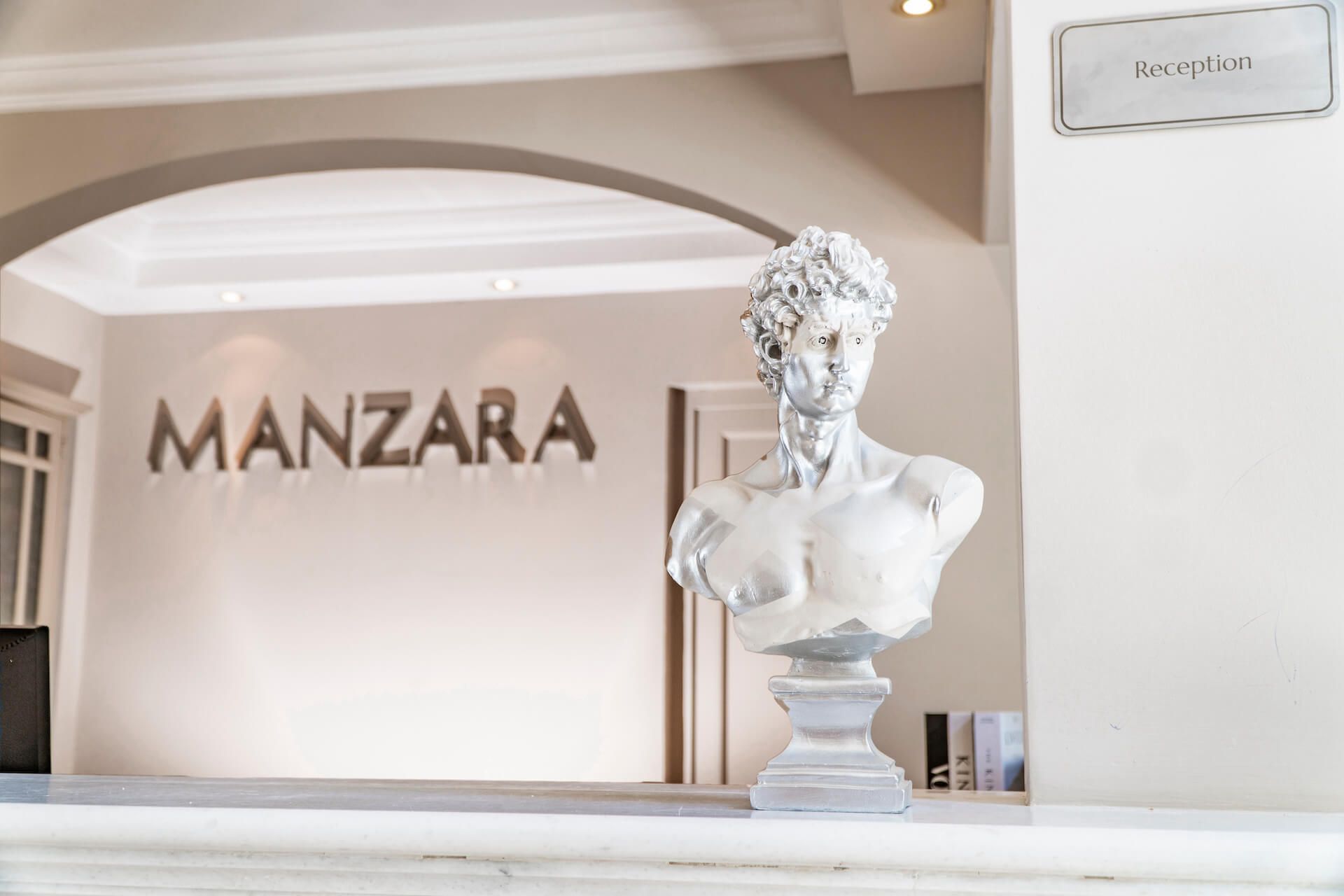 A statue of a man is sitting on a counter in front of a sign that says manzara.