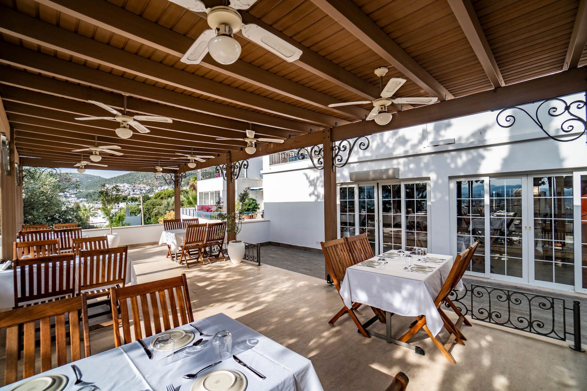 A restaurant with tables and chairs under a pergola with ceiling fans.
