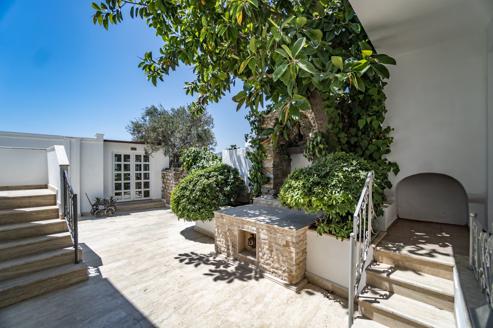 A white house with stairs leading up to it and a table under a tree.