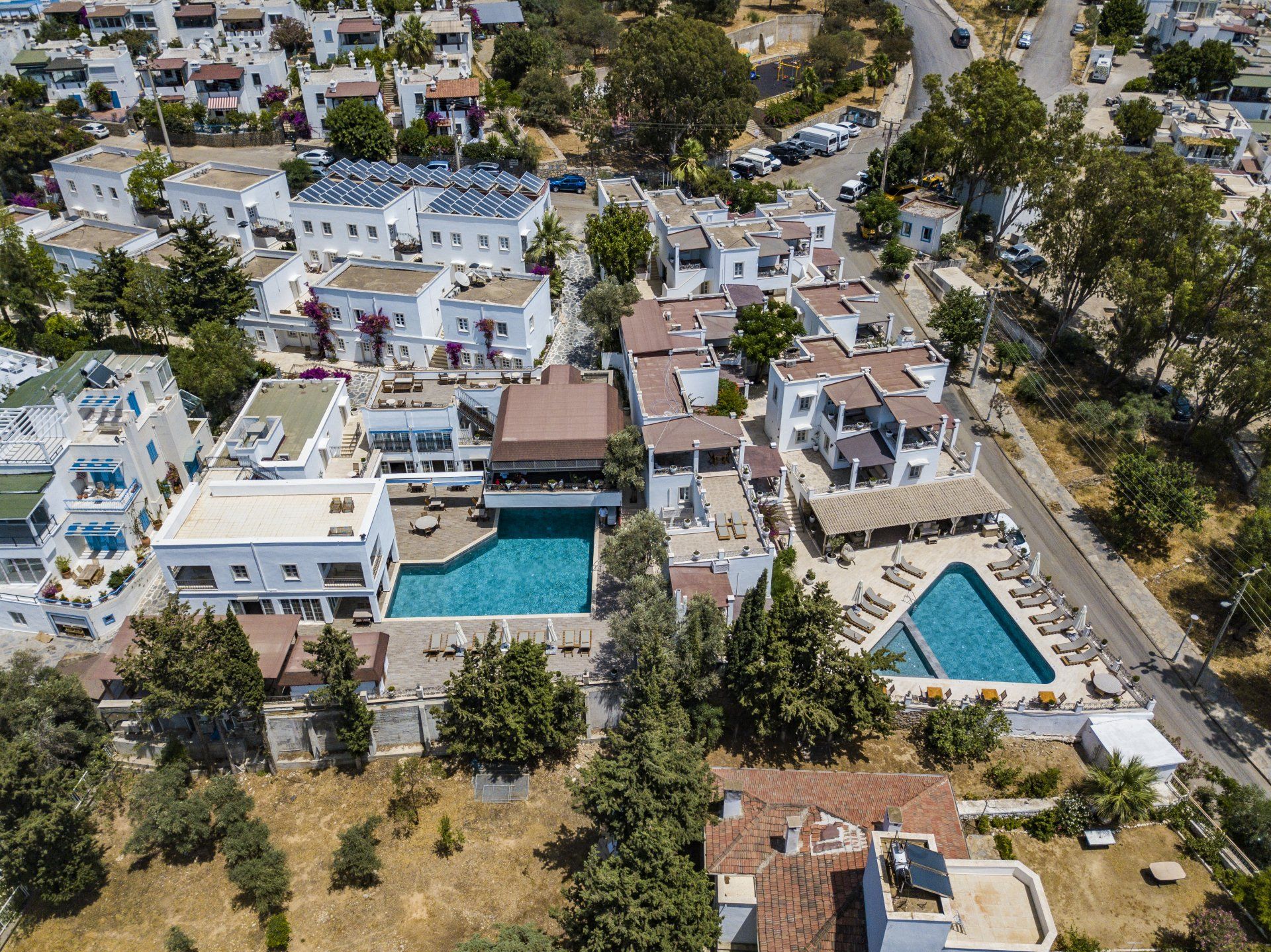 An aerial view of a hotel with a large swimming pool surrounded by buildings and trees.