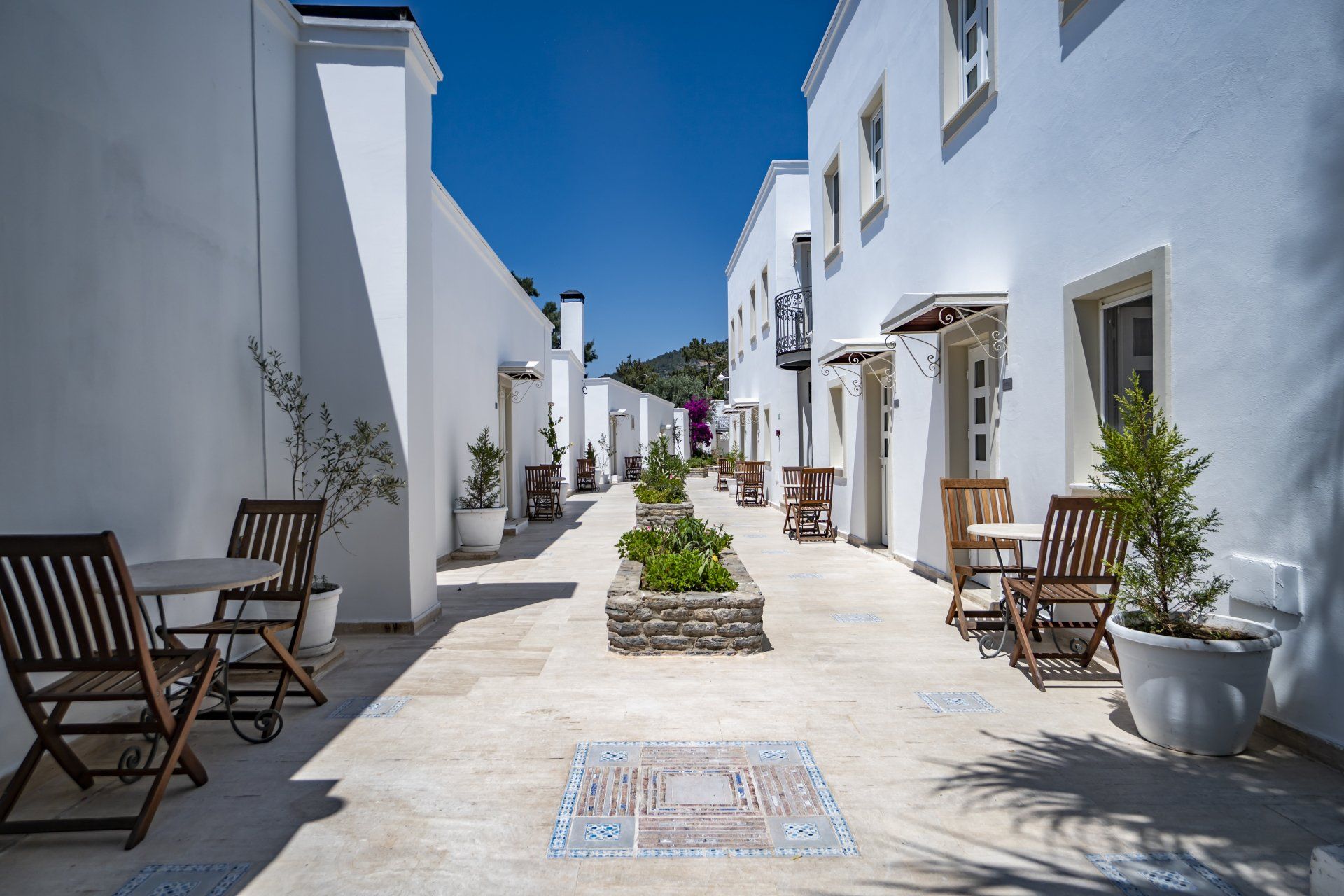 A narrow alleyway between two white buildings with chairs and tables.