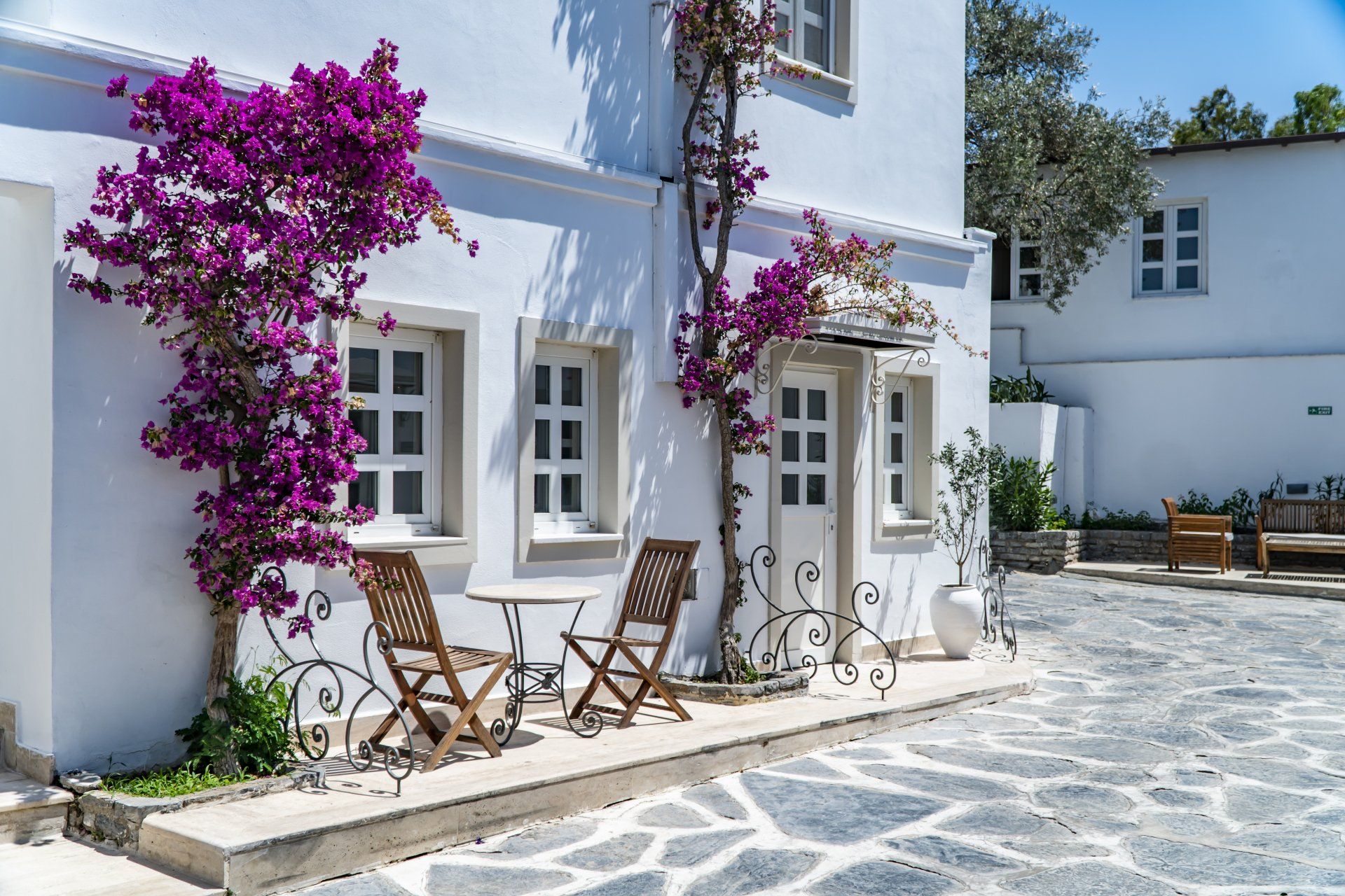 A white building with purple flowers and chairs in front of it