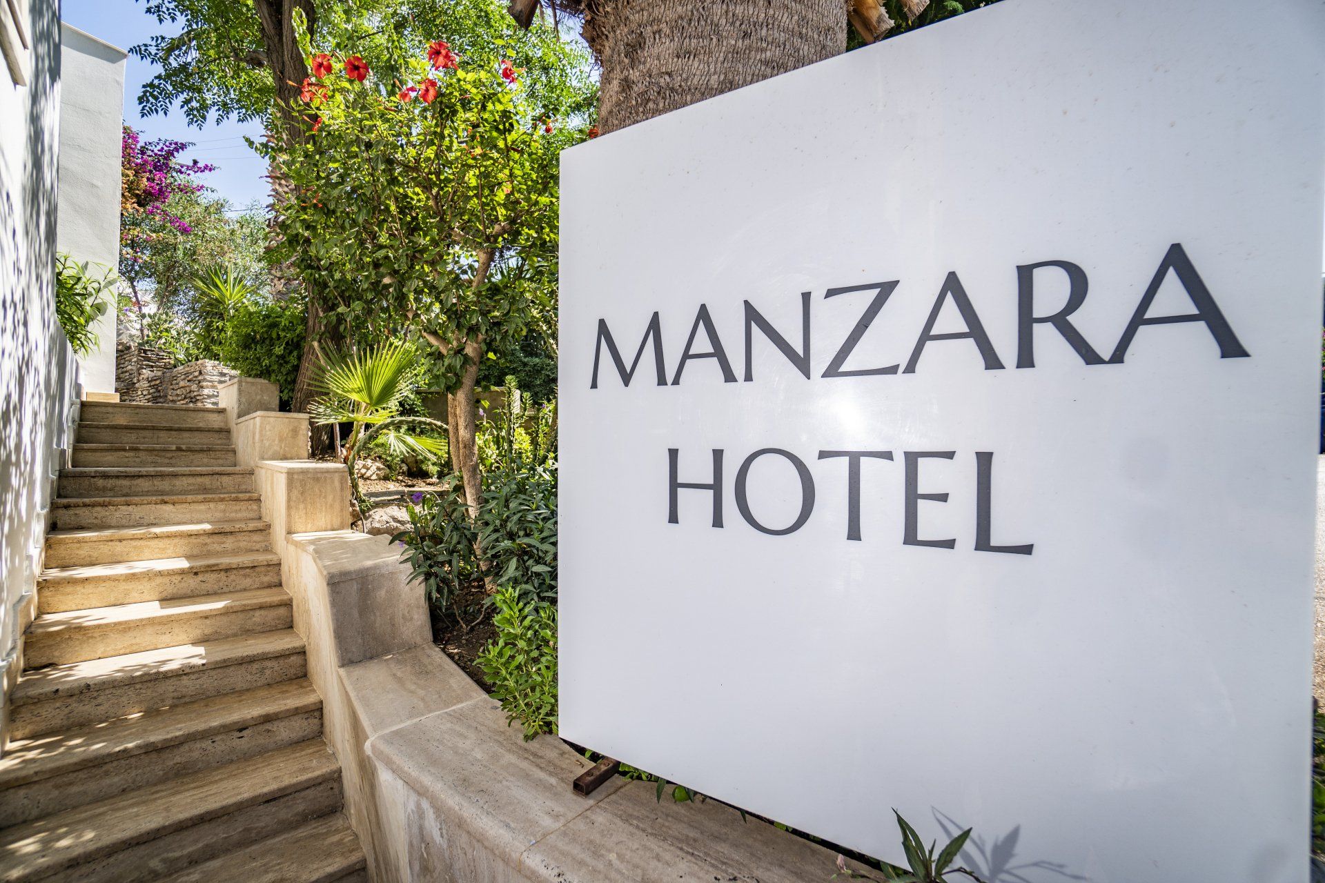 A white sign that says manzara hotel is sitting next to a set of stairs.