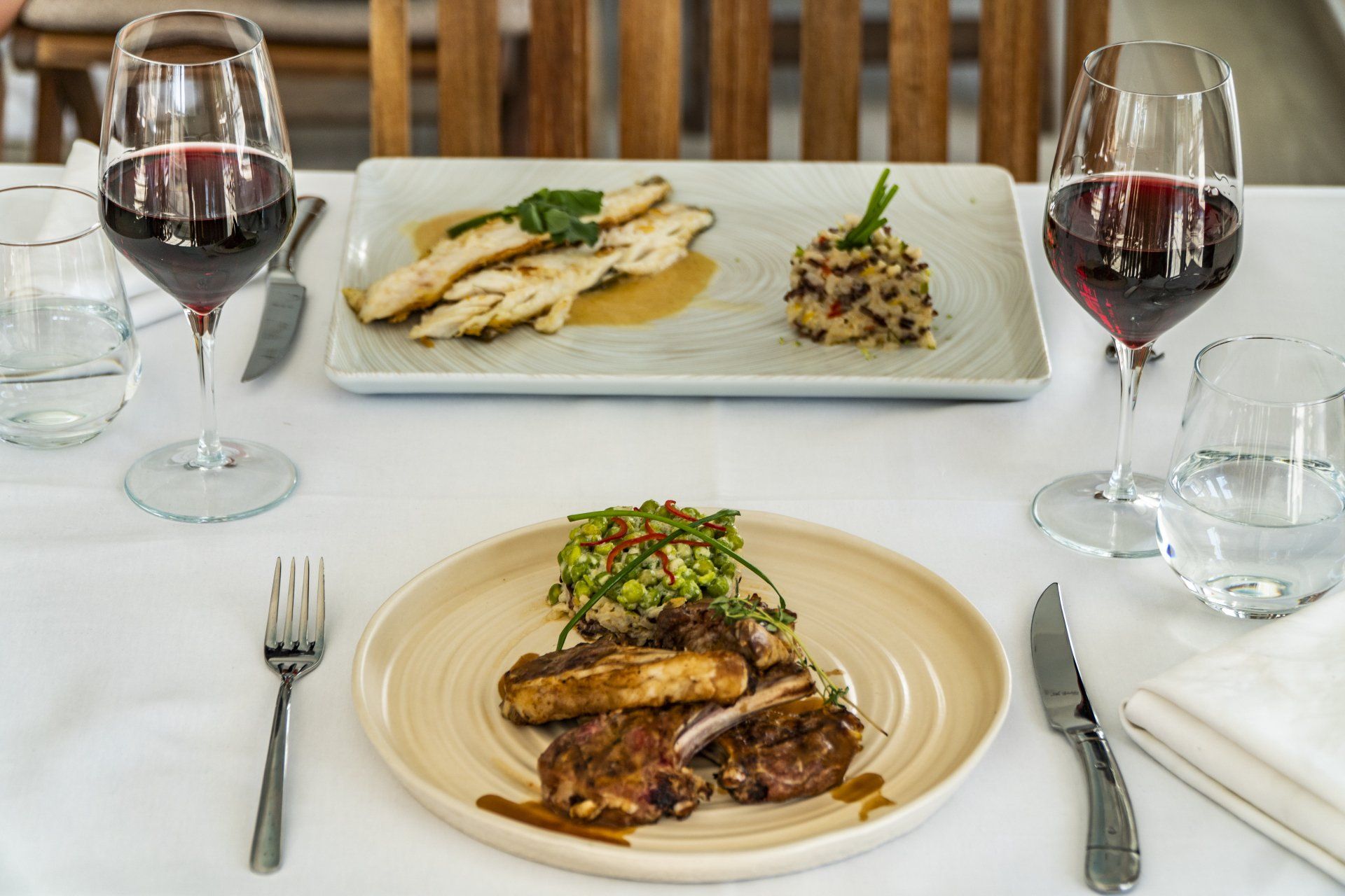 Two plates of food and two glasses of wine on a table.