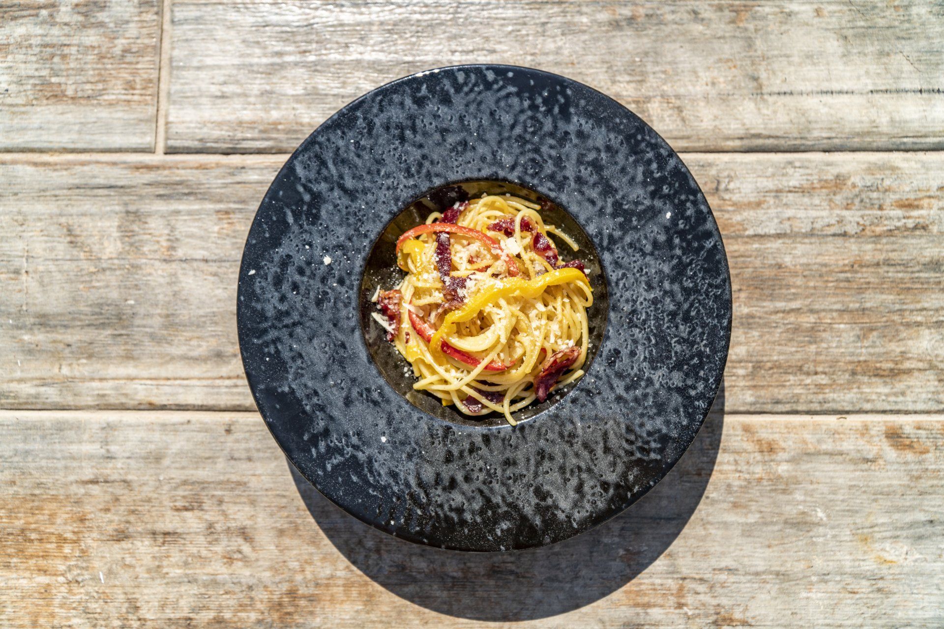 A black plate topped with spaghetti and meat on a wooden table.