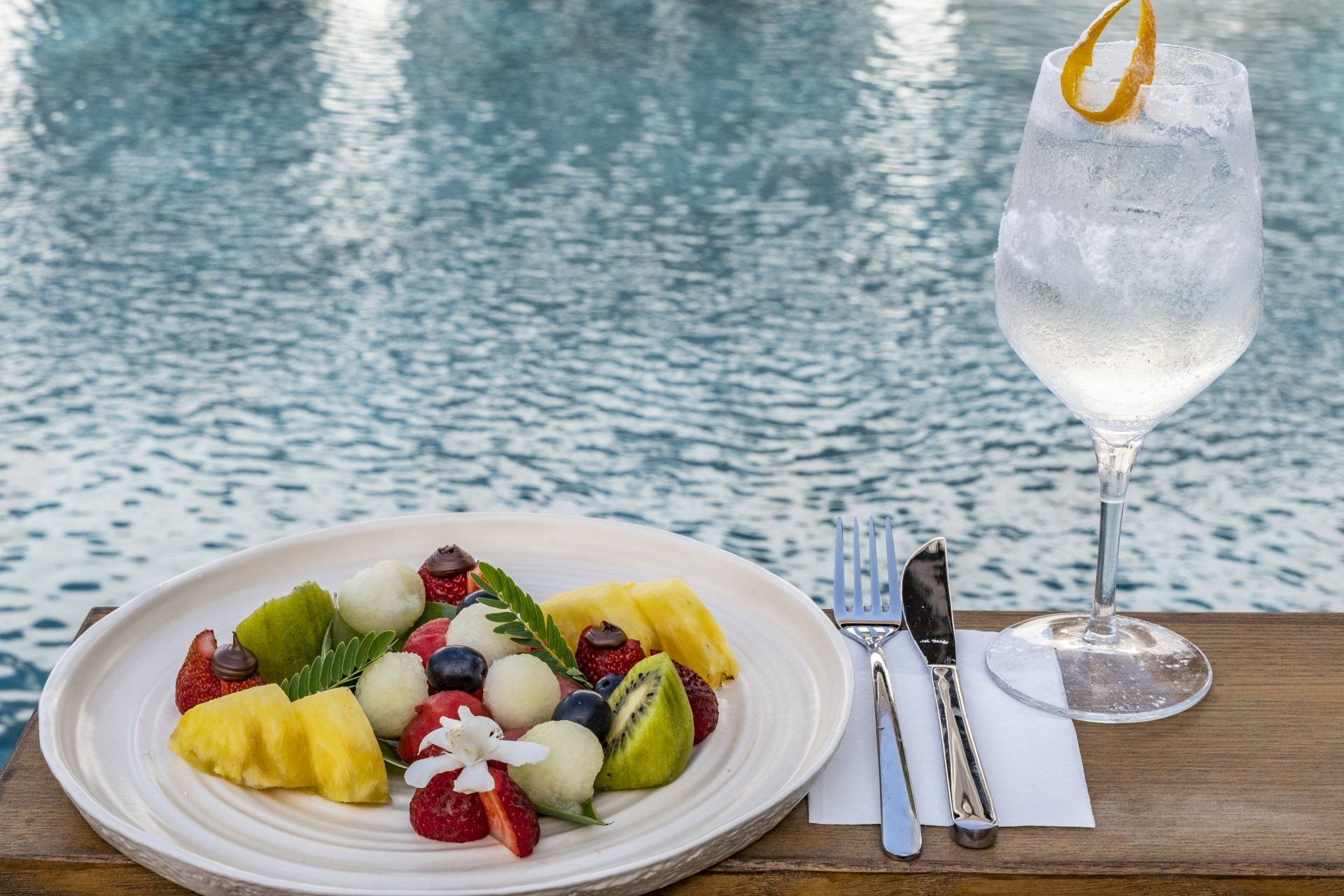 A plate of fruit salad next to a glass of water.