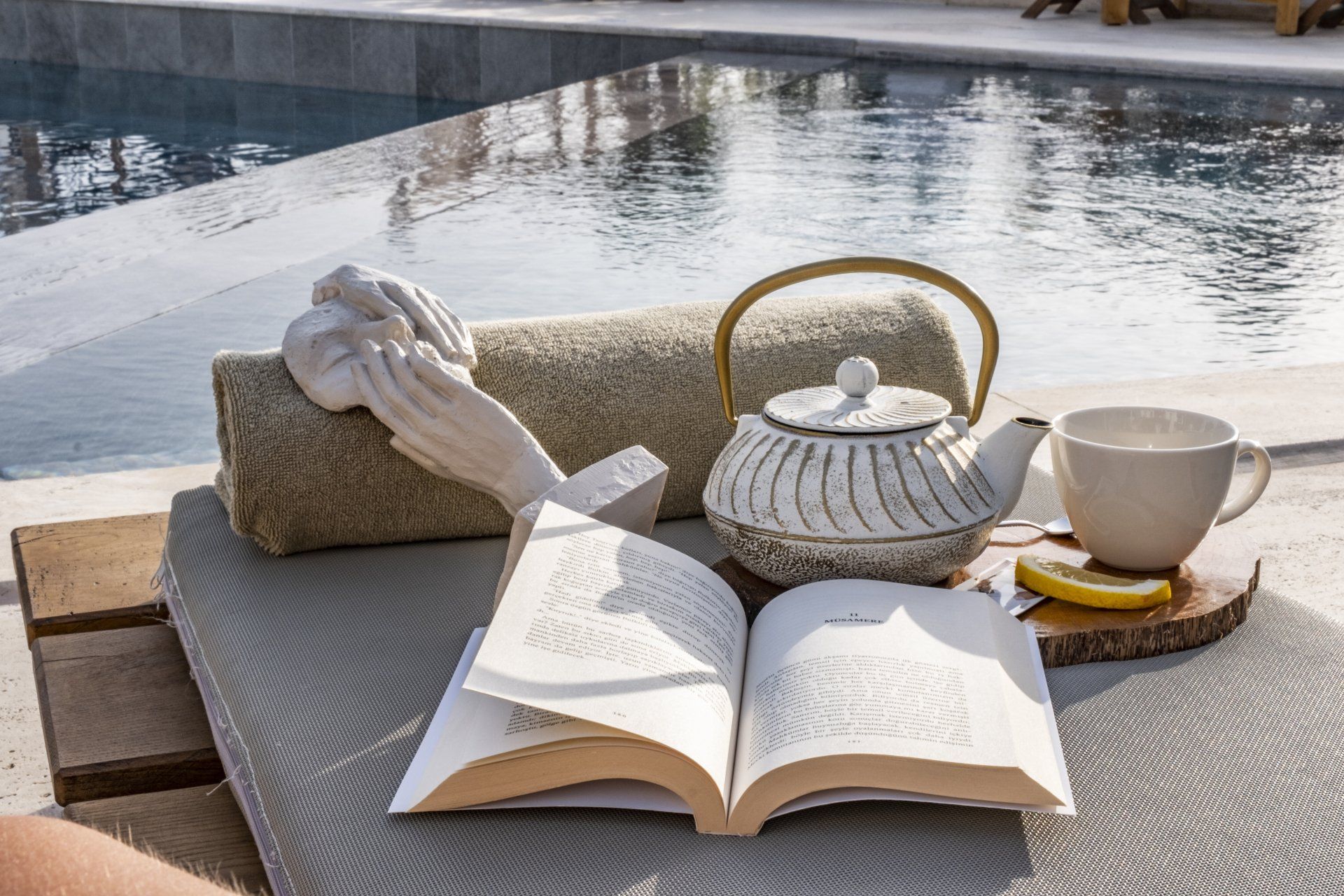 A person is reading a book next to a teapot and a cup of tea.