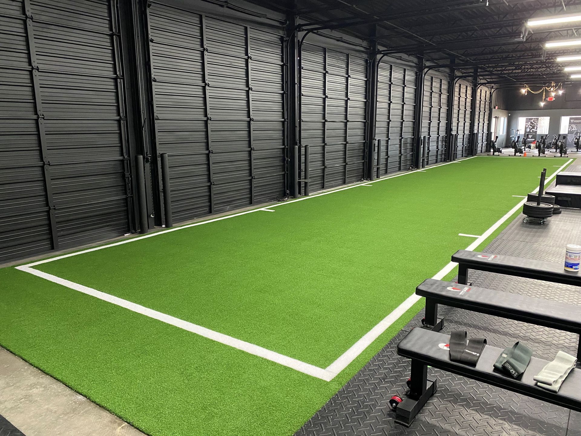 Gym interior with green turf track, black walls, and weight equipment.
