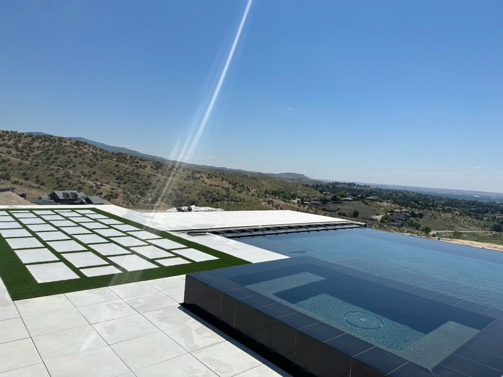 Infinity pool overlooking a landscape with a tiled patio and a hot tub; sunny day.