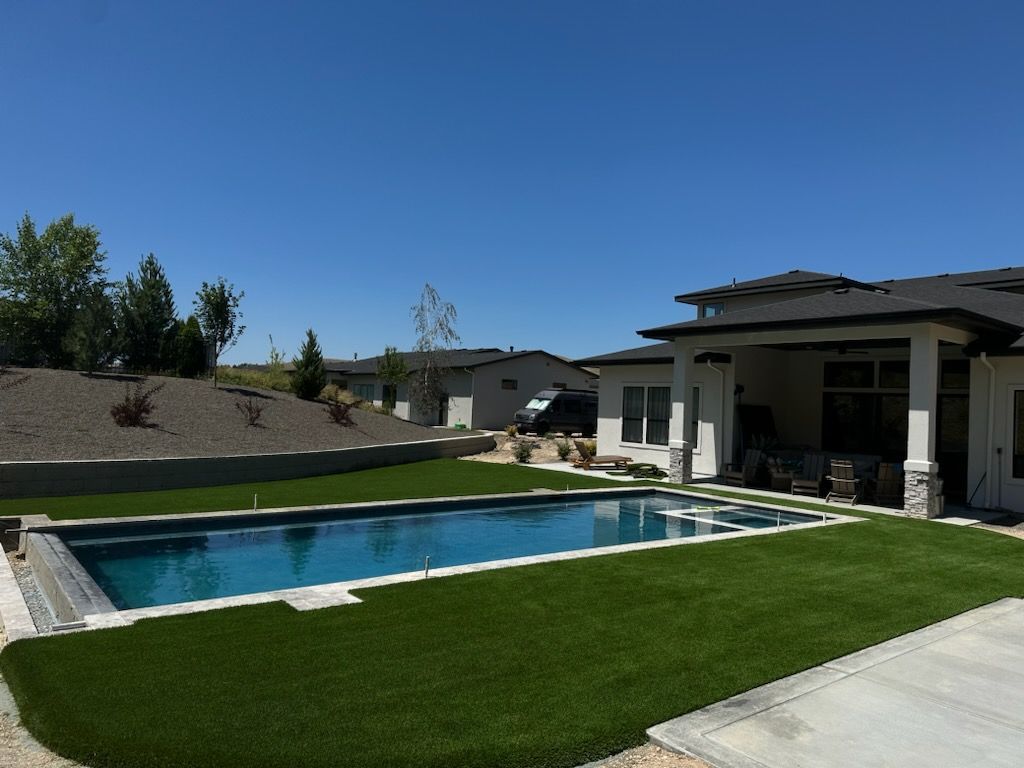 Backyard with pool, artificial grass, and house under a blue sky.