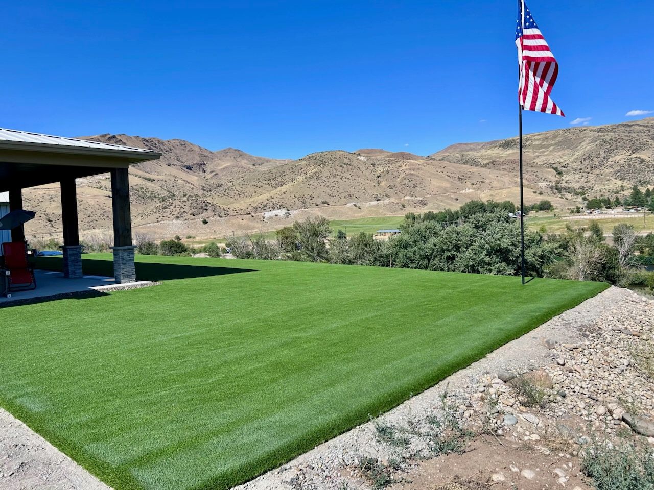 Green artificial turf, pavilion, American flag, mountains, and blue sky.