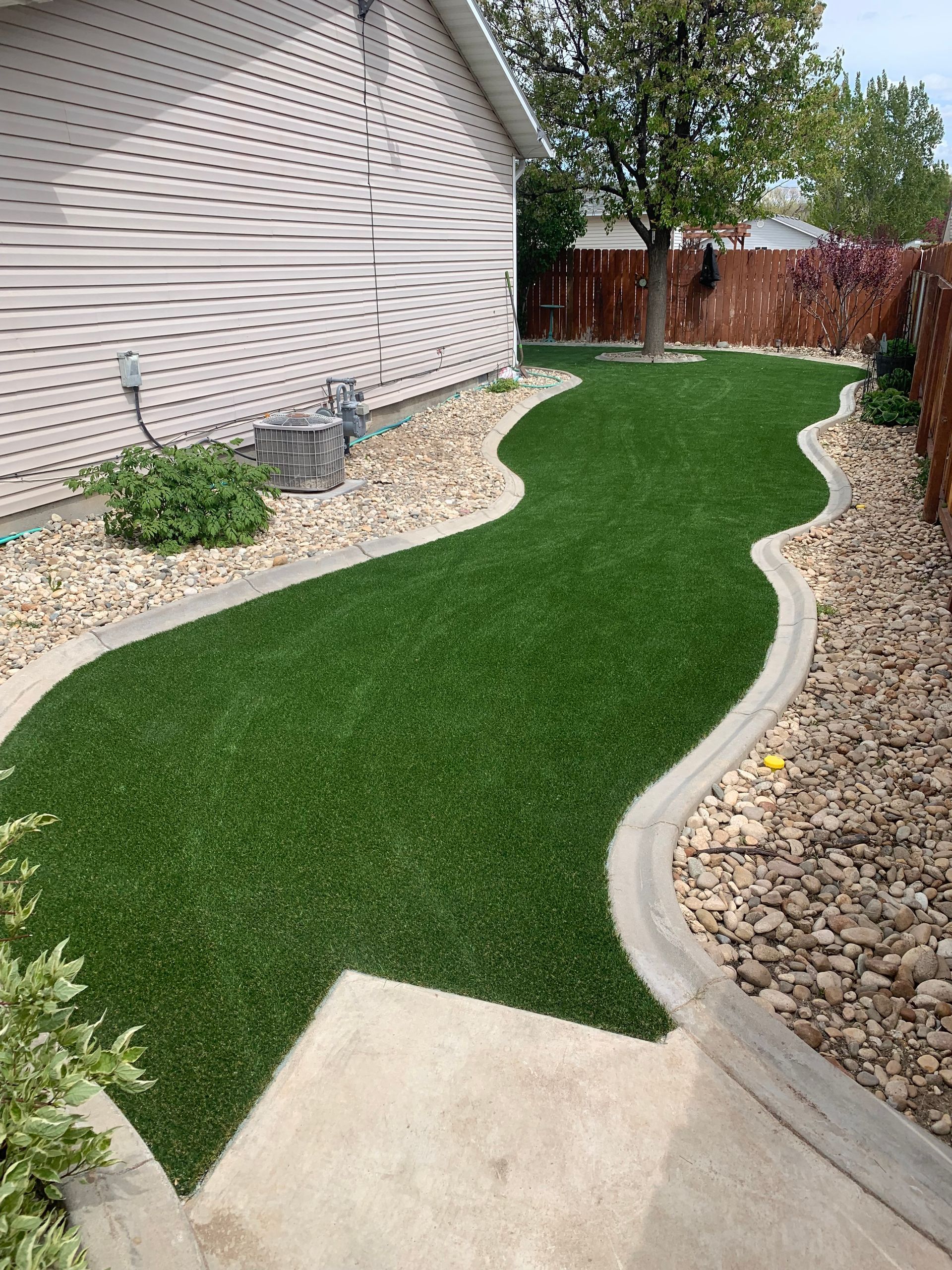 Artificial turf path with concrete borders next to a house with rock landscaping.