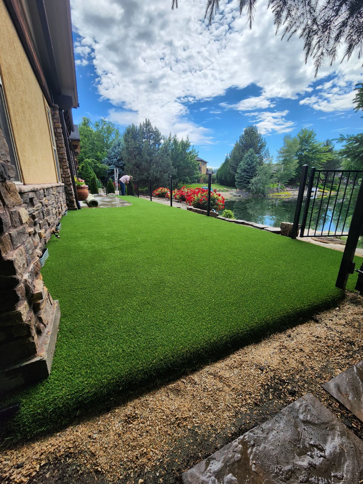 Green artificial turf lawn next to a building and water feature with blue sky.