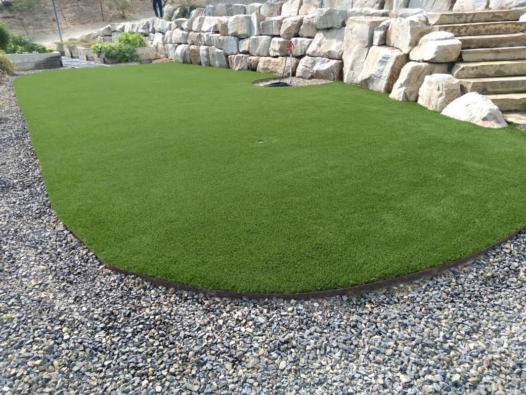 A patch of green artificial turf is surrounded by small stones and a rocky retaining wall.