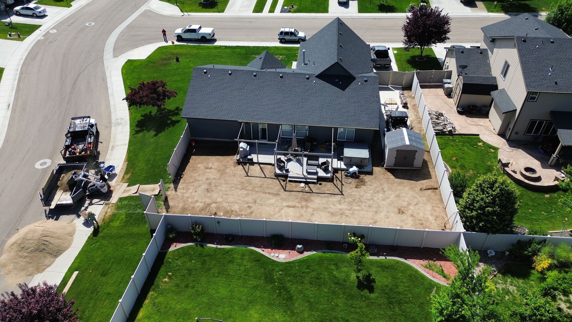 Overhead view of house with gray roof, back patio, fenced yard. Construction equipment next to driveway.