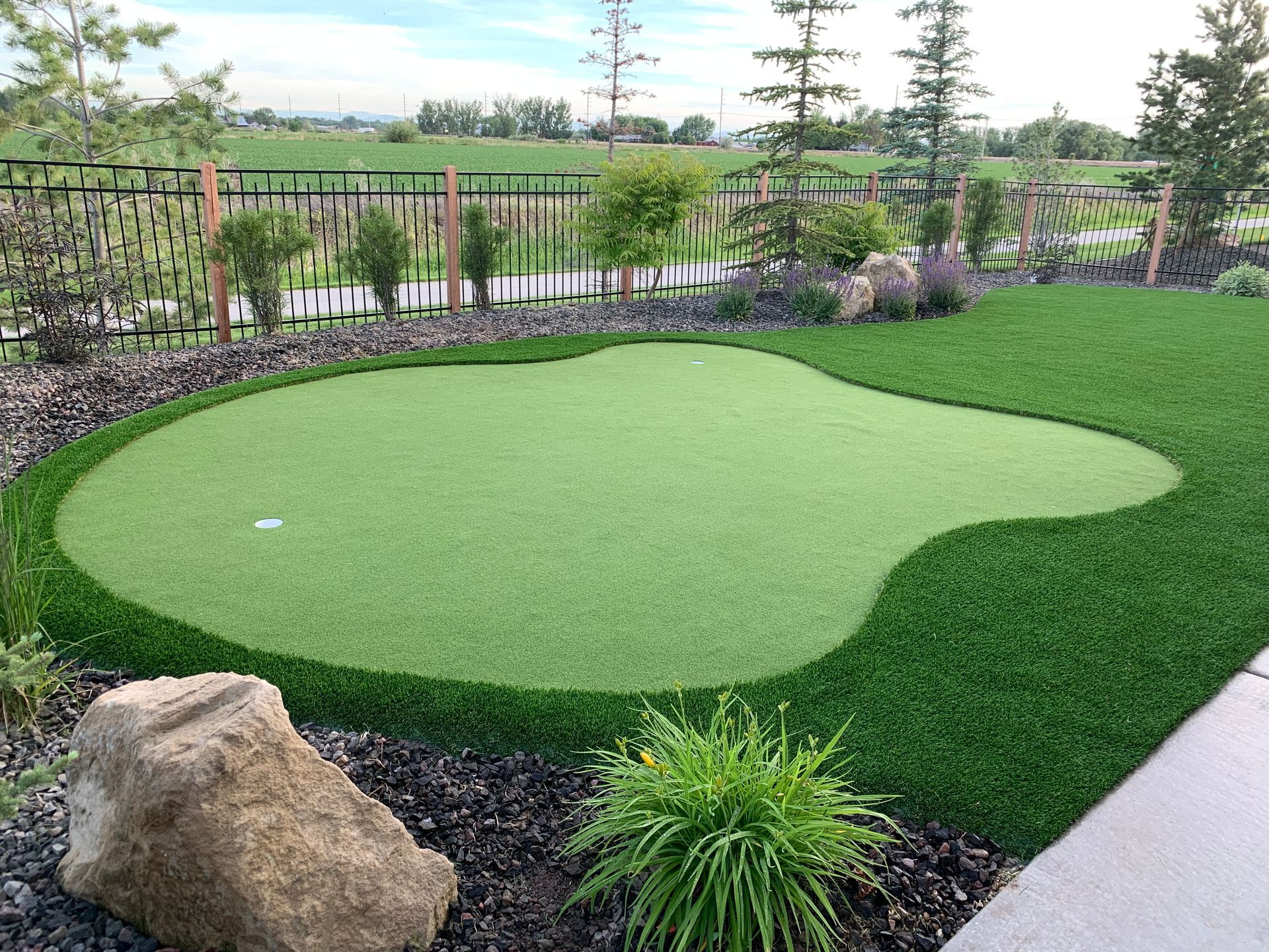 Putting green with artificial turf, surrounded by landscaping and fence.