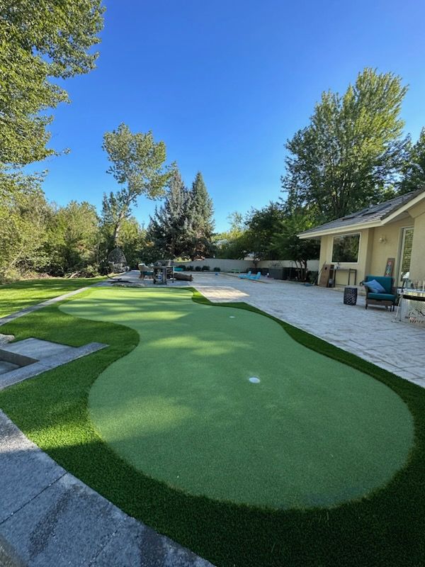 Green putting green with a golf hole in a backyard with a patio.
