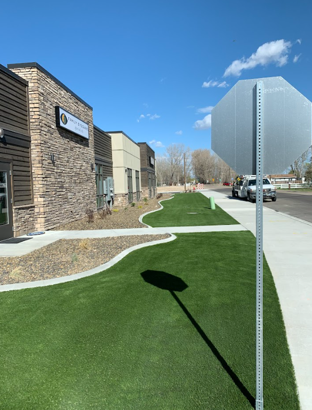 Building with a sign, lush green lawn, sidewalk, and stop sign on a sunny day.