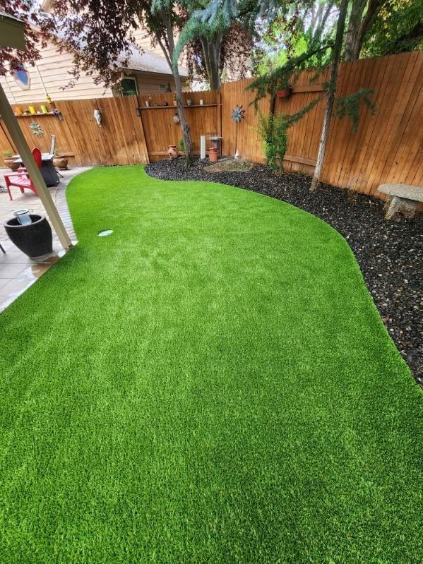 Green artificial lawn in a backyard, with a wooden fence and black mulch border.