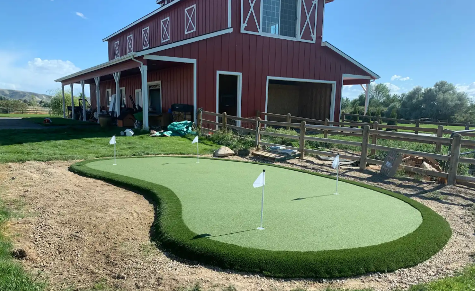 A backyard putting green with white flags, in front of a red barn-style building.