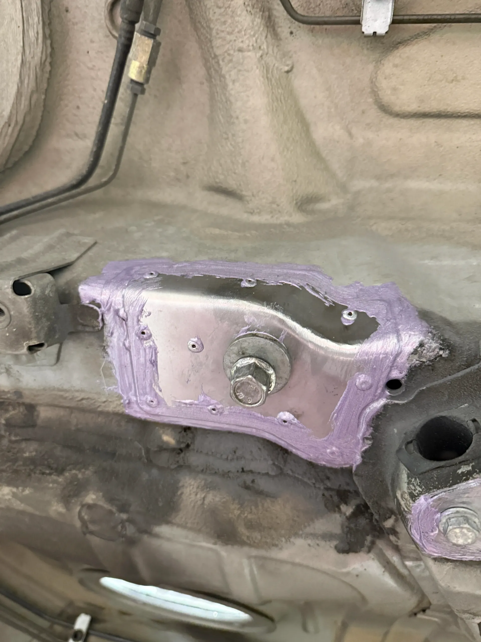 Silver metal bracket with a bolt, attached to a car's undercarriage, sealed with purple sealant. | GermanTech MotorWorks, LLC