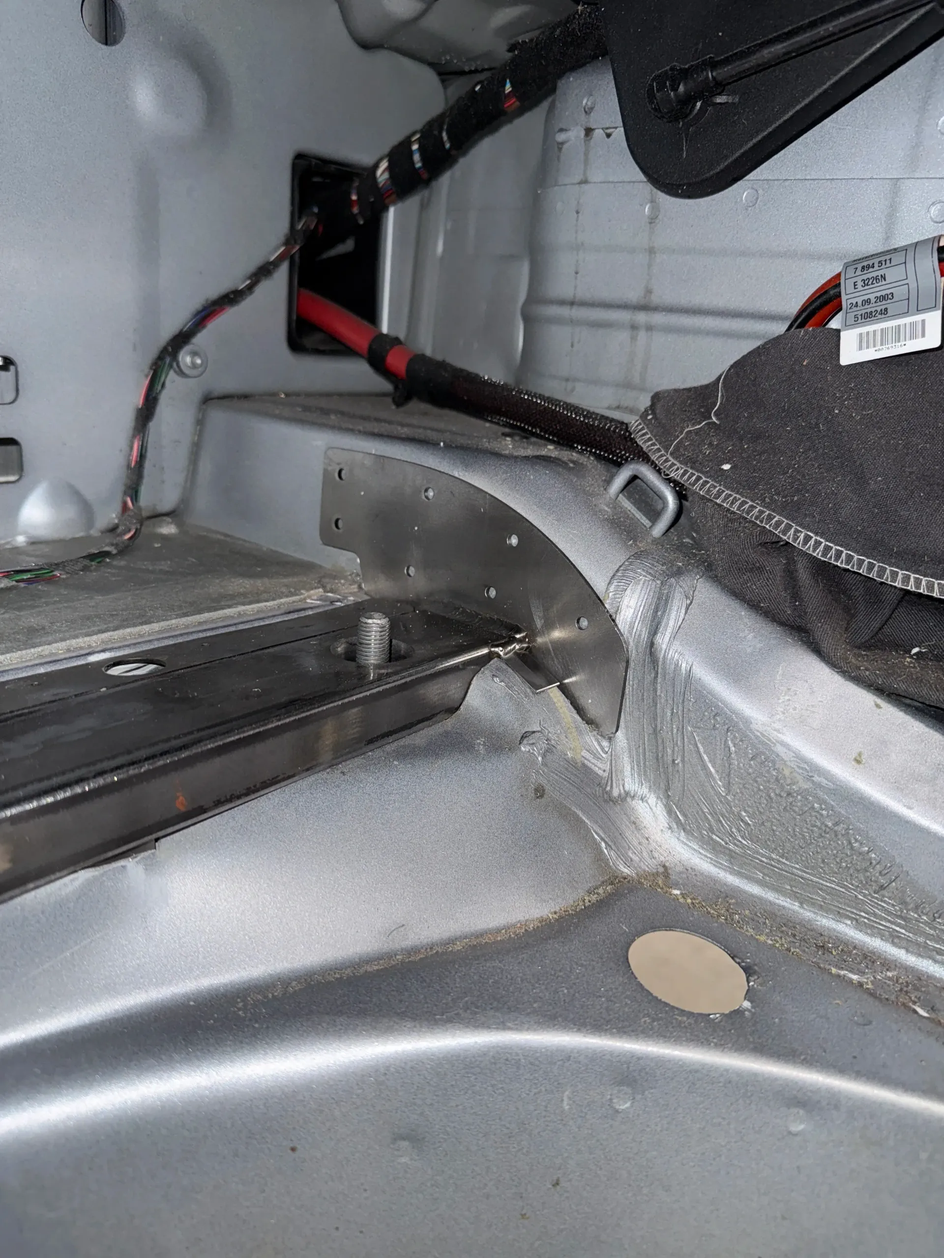 Inside of a car's trunk, showing wiring, metal frame, and a black box. The interior is silver. | GermanTech MotorWorks, LLC