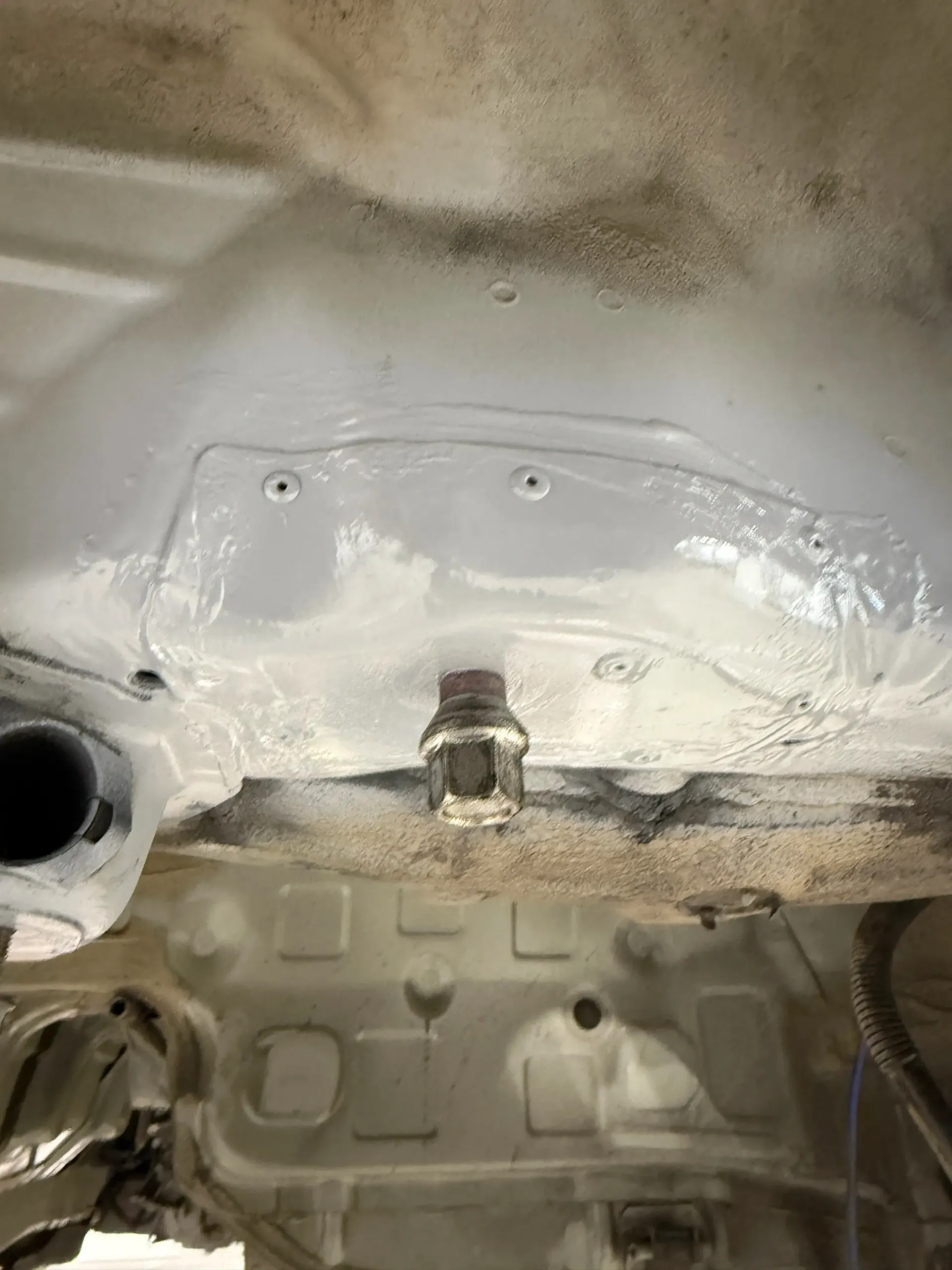 Underside of a car body painted white, showing a large metal nut and various holes. | GermanTech MotorWorks, LLC