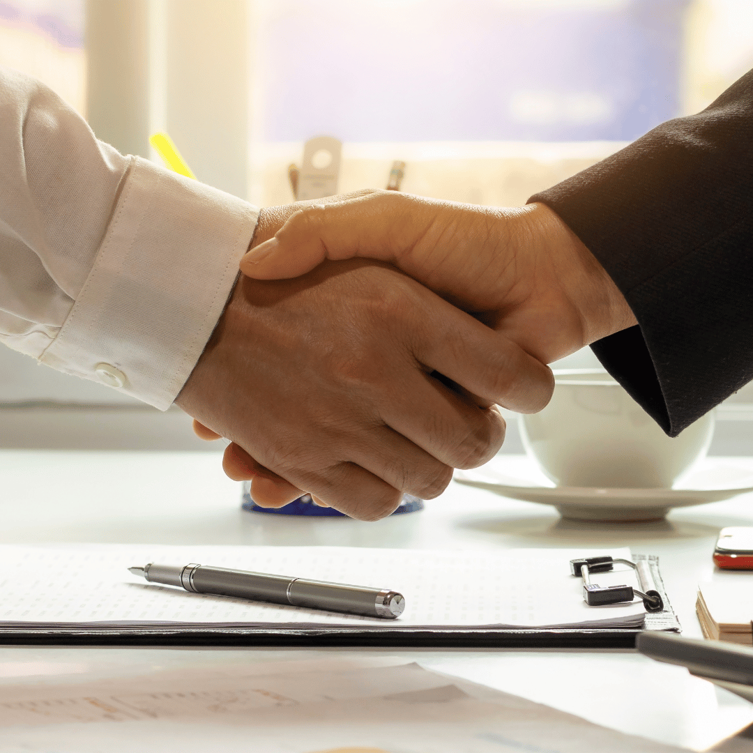 A man in a suit shakes hands with another man in a white shirt