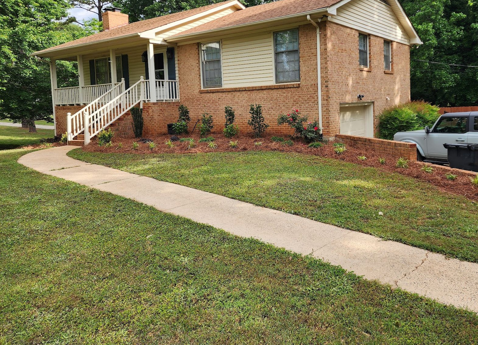 Brick house with a concrete walkway, porch, and landscaped flower beds.