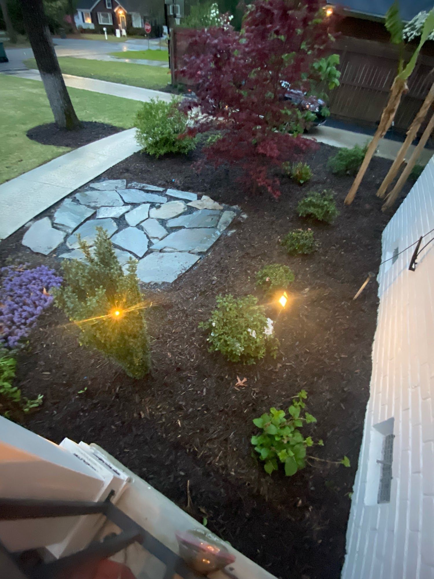 A well-landscaped front yard with a stone path, plants, and string lights. Evening setting.