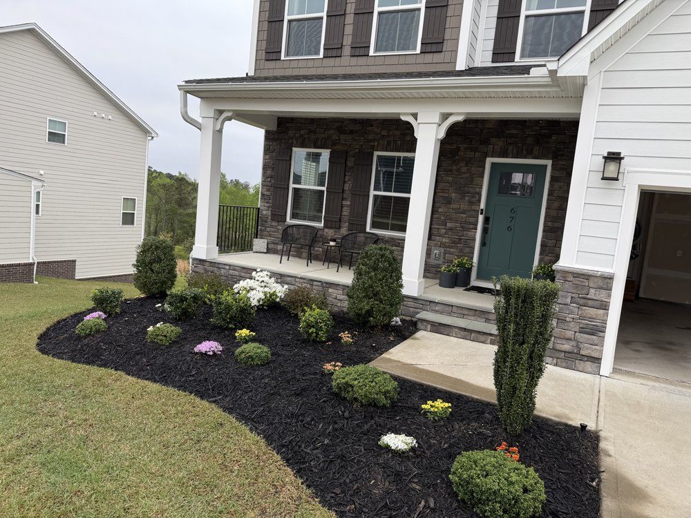 Front yard landscaping with black mulch, green shrubs, and a house with a stone facade.