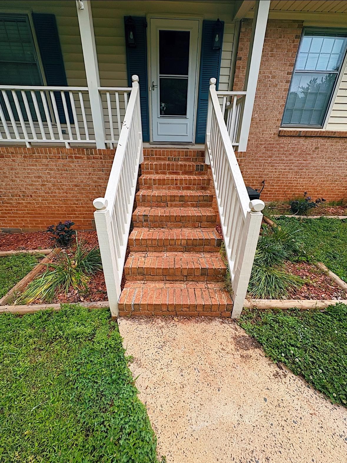 Brick steps with white railings leading to a house's front door; grass and landscaping surround.