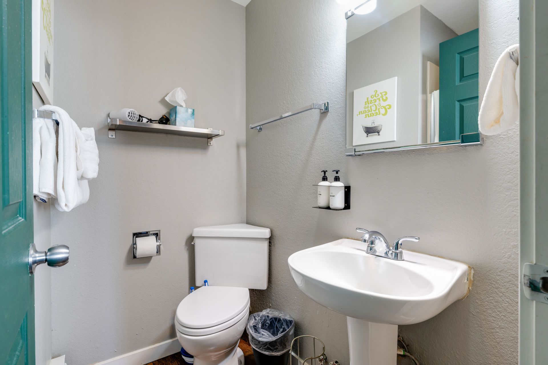 Small bathroom with gray walls, white toilet, pedestal sink, teal door.