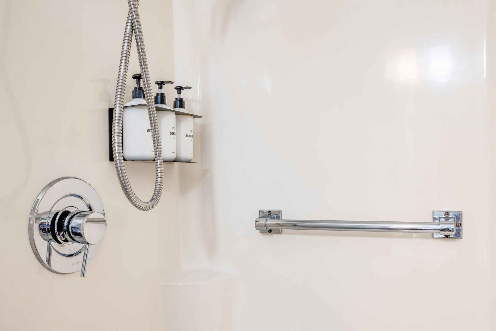 Shower interior with chrome fixtures, shampoo bottles, and a grab bar.