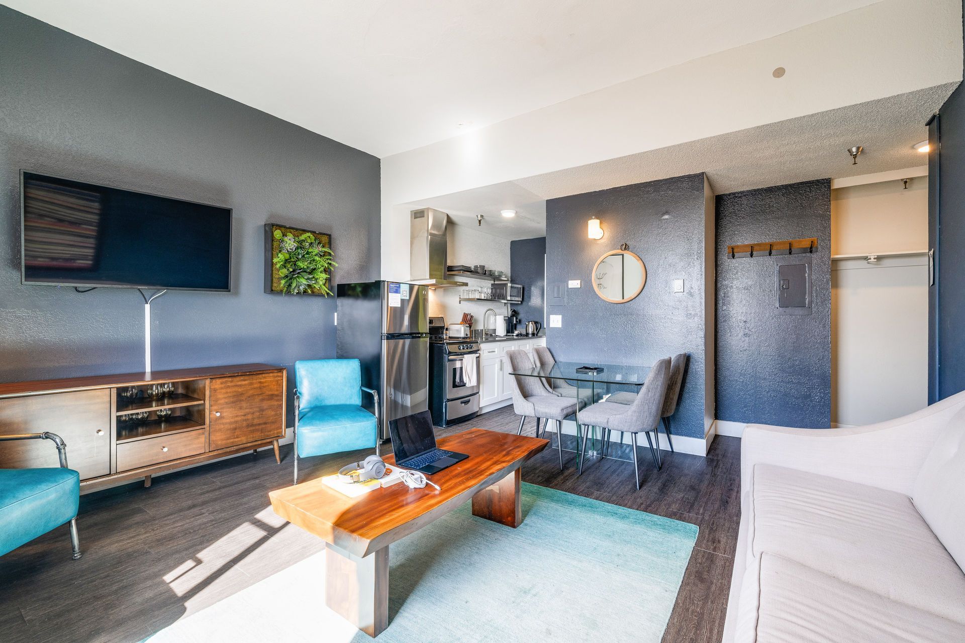 Modern apartment living room with teal accents, open kitchen, and TV.
