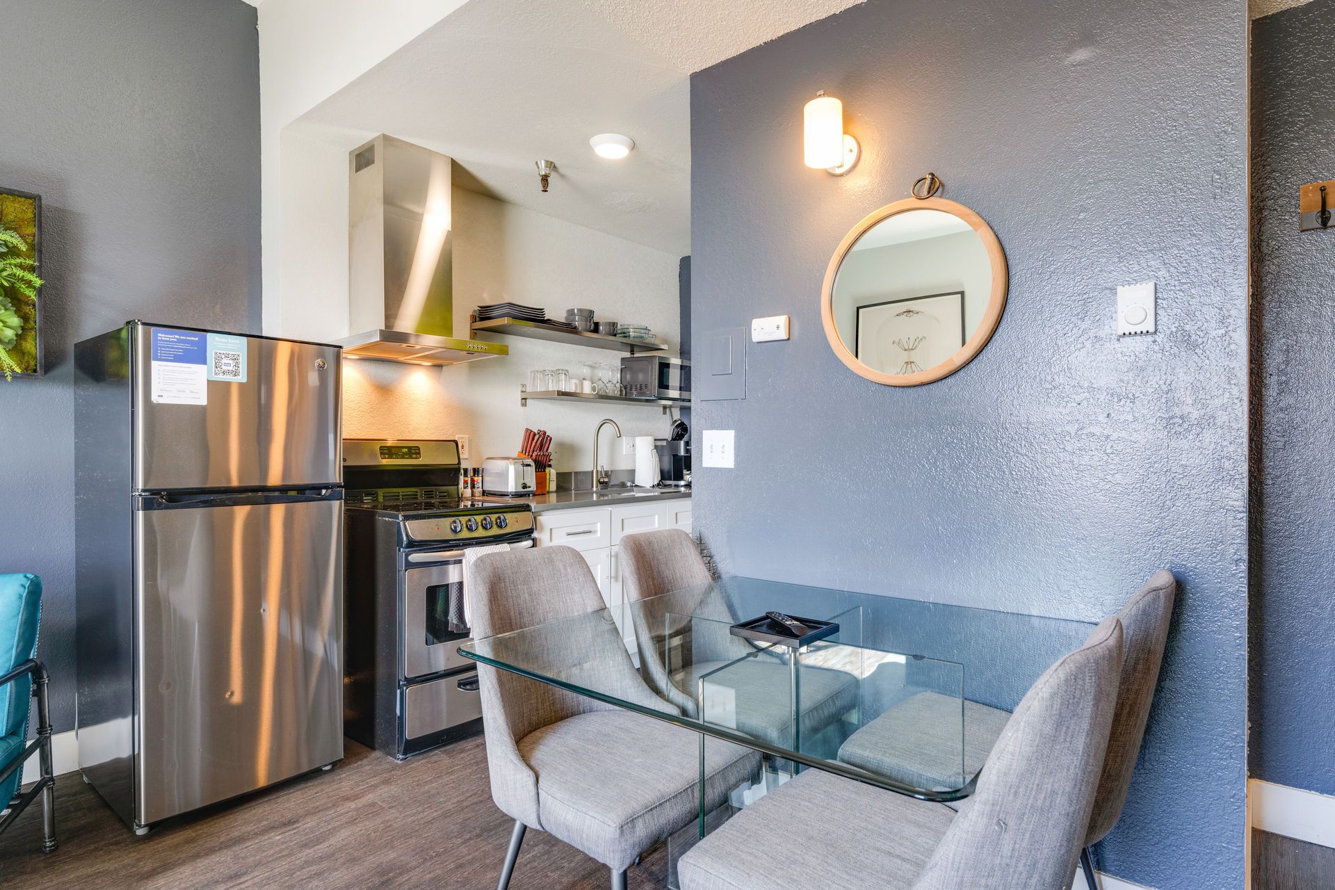 Small kitchen and dining area with stainless steel appliances, glass table, and gray walls.