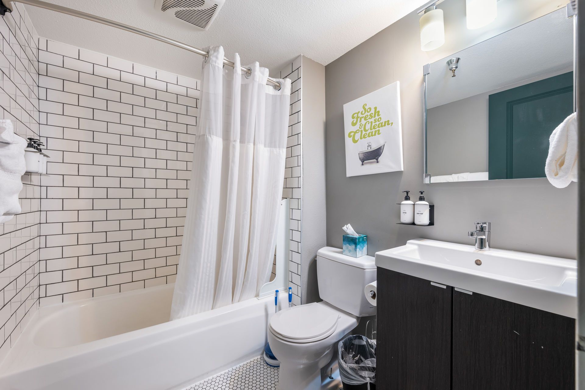 Bathroom with white subway tile, a bathtub, toilet, vanity, and a gray wall.