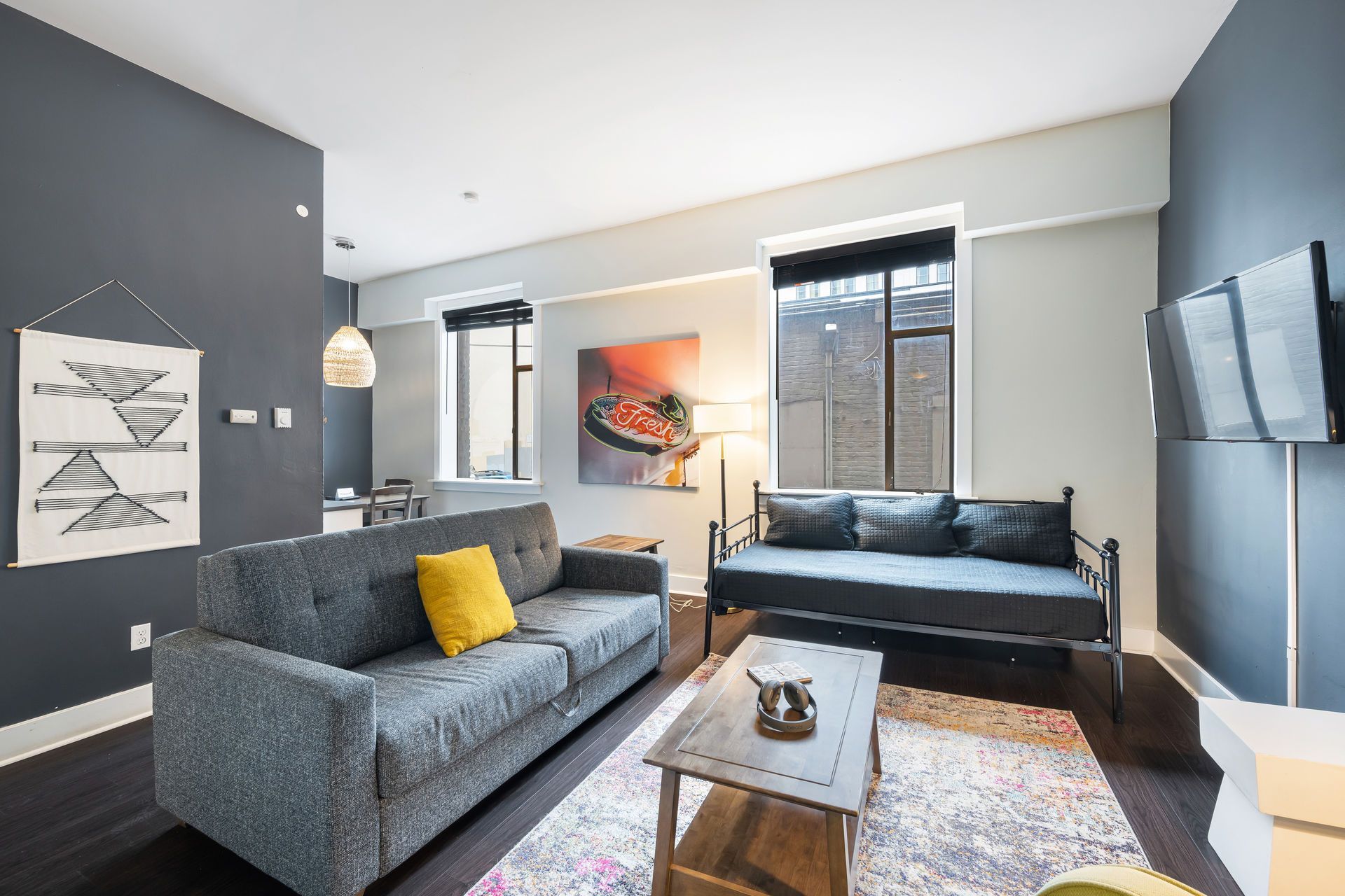 Gray living room with sofa, daybed, art, rug, and dark wood floors.