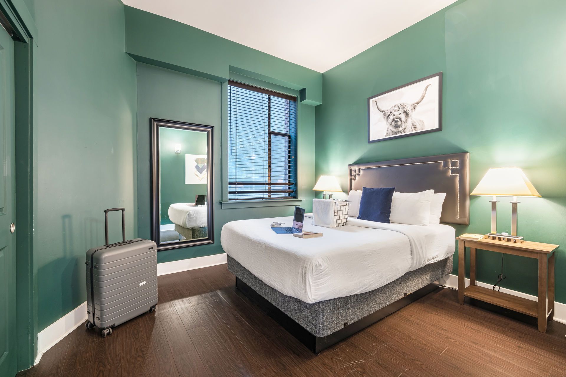 Hotel room with a bed, luggage, mirror, lamps, and green walls.