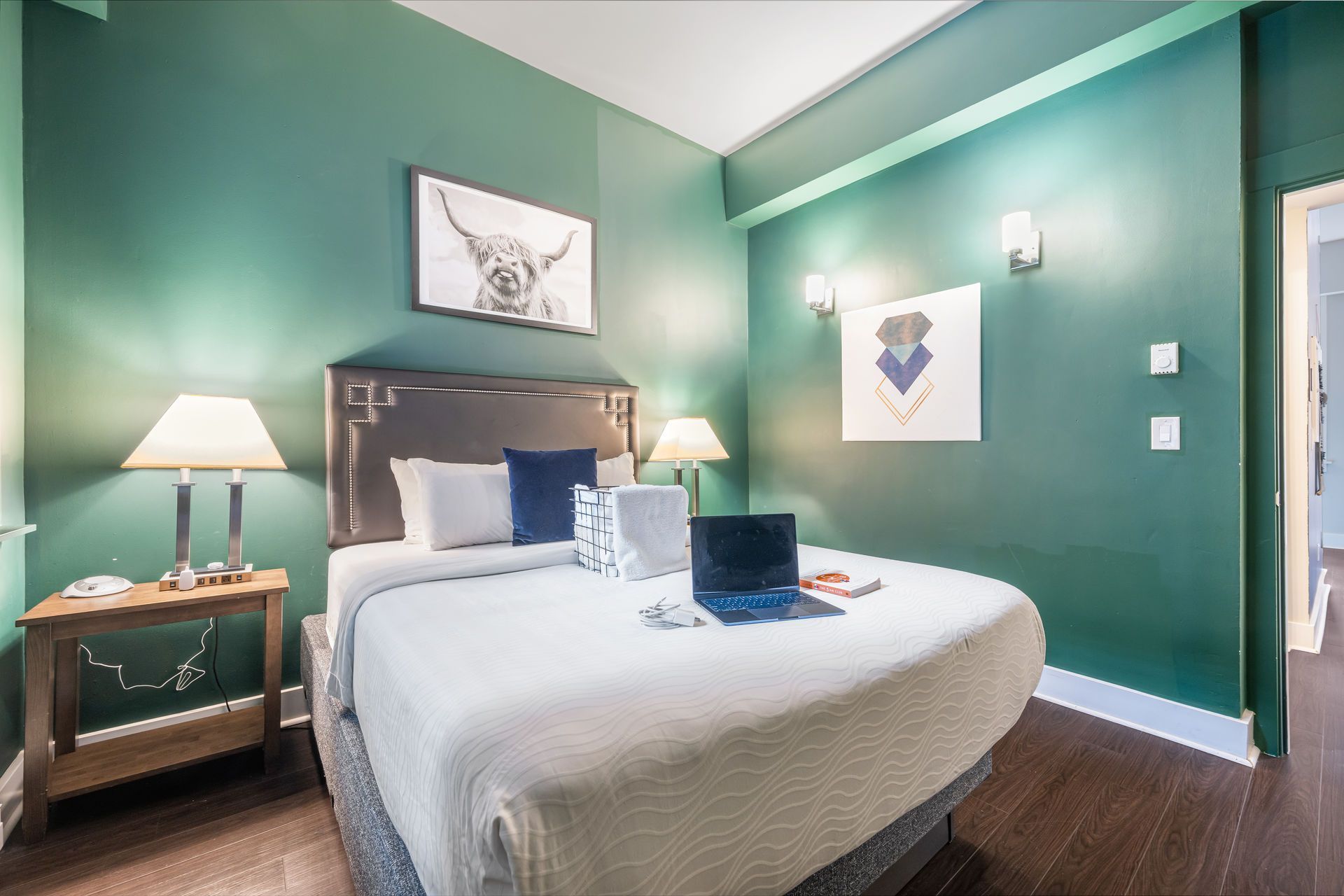 Green bedroom with a bed, artwork, lamps, and a laptop.