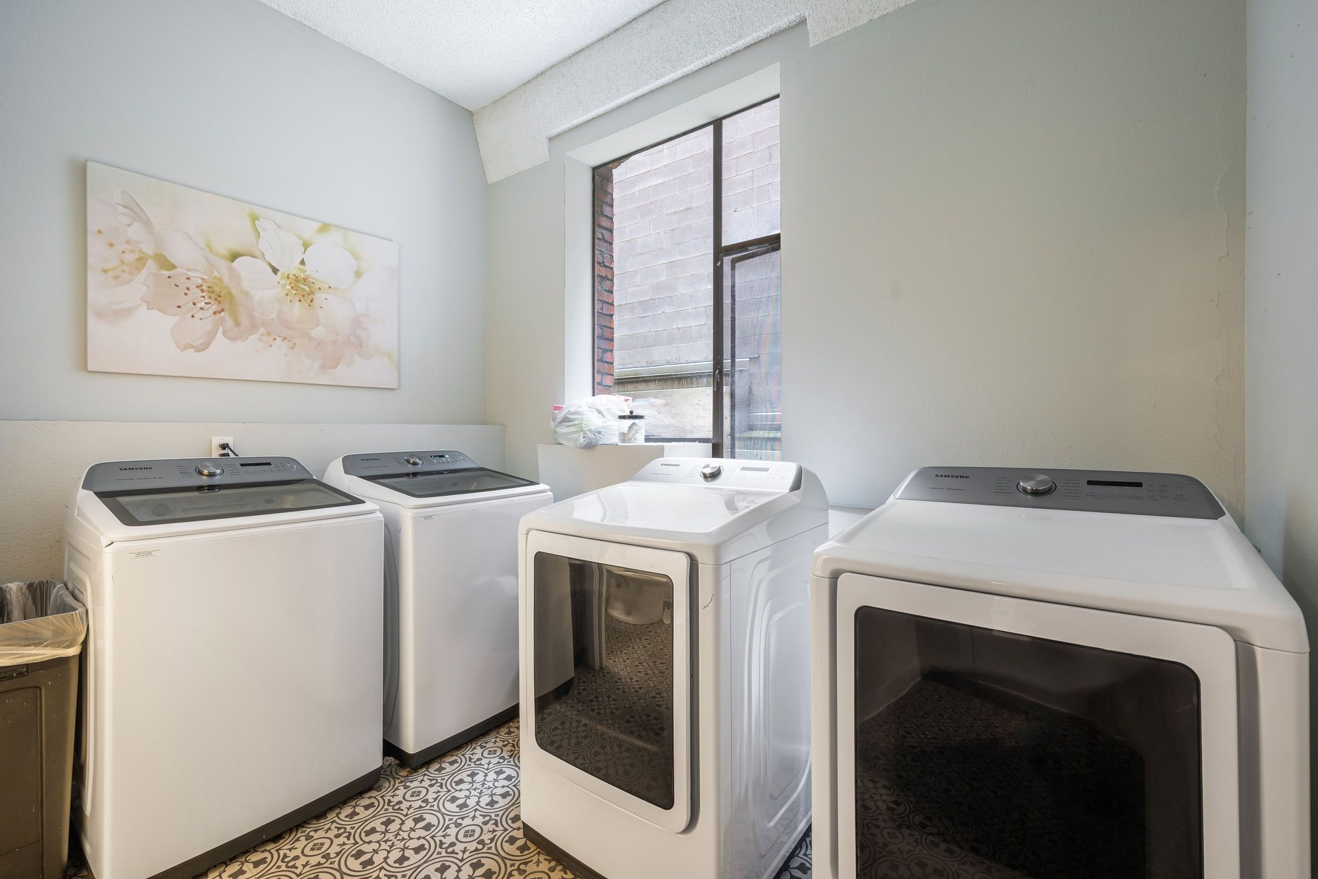 Laundry room with four white washers and dryers, art, and a window.