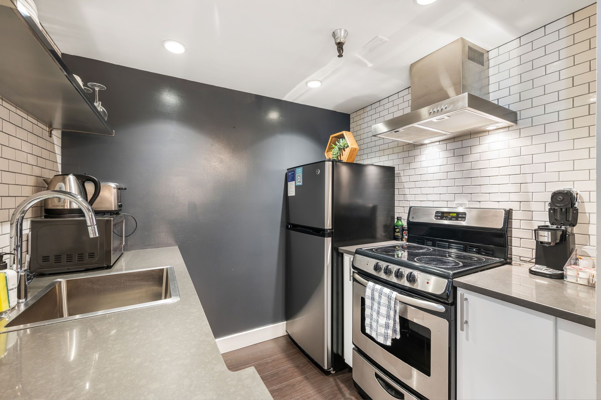 A small modern kitchen with dark gray walls, stainless steel appliances, and white brick tile.