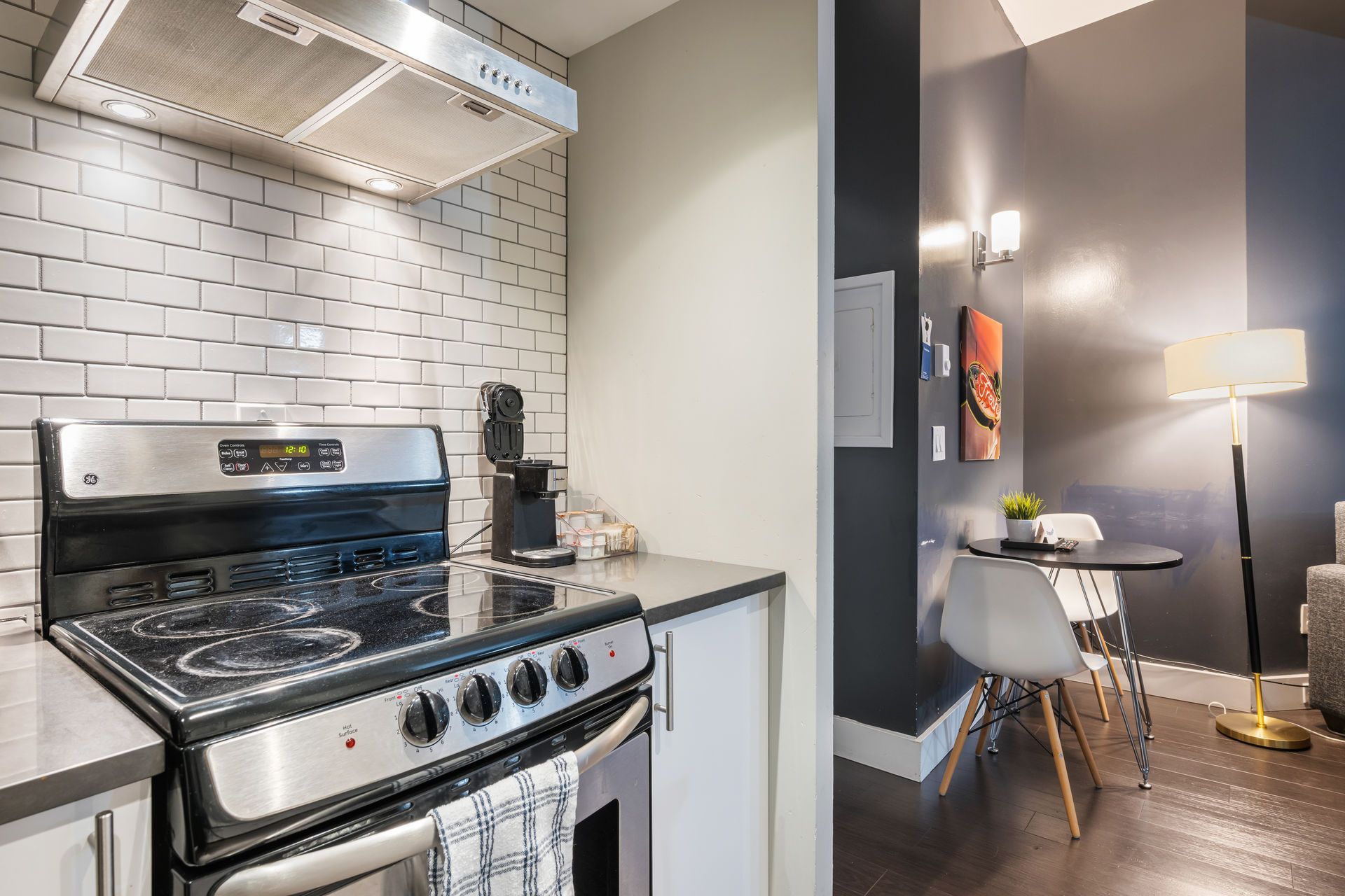 Modern kitchen with stainless steel appliances and partial view of a dining area with round table and chair.