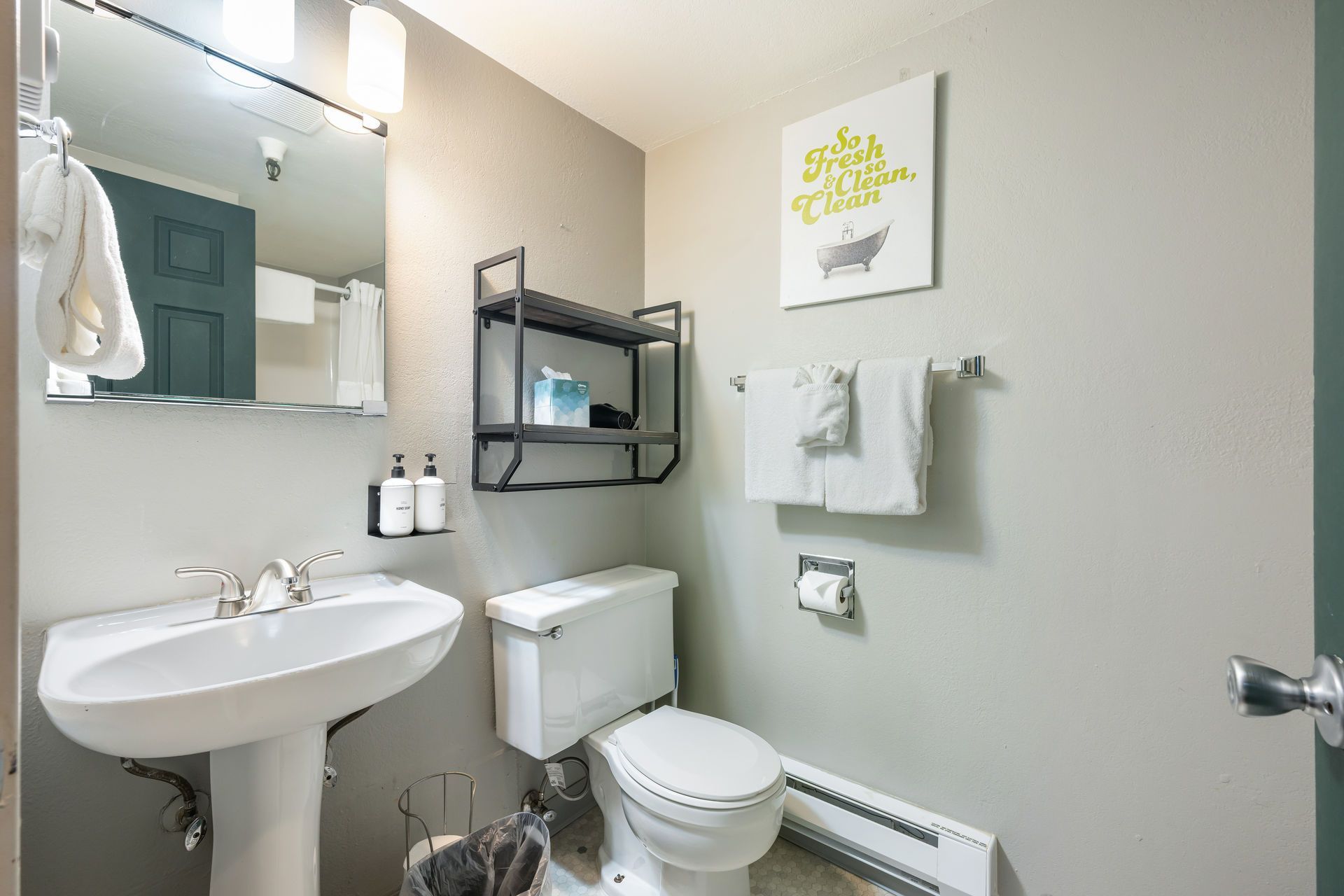 Small bathroom with a pedestal sink, toilet, shelving, and a small painting.